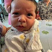 Alexander is registered to the contest to win money with this photo: baby, infant, person, face, clothing, pineapple_pattern, indoor, table, tablecloth, plant_pattern, adult, woman, holding, portrait, expression, closeup, family, casual, furniture, room