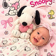 Elena is registered to the contest to win money with this photo: baby, blanket, bow, cartoon, child, close_up, dog_toy, flowers, happy, headband, hearts, indoor, infant, lying_down, pajamas, pink, plush_toy, portrait, smiling, snoopy