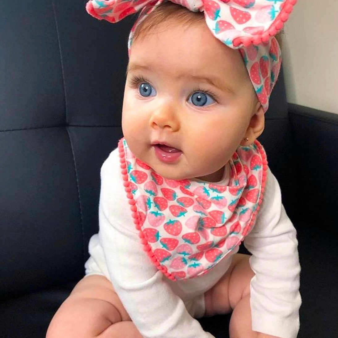 Mia participe au concours pour gagner de l'argent avec cette photo : baby, blue_eyes, headband, strawberry_pattern, bib, white_clothing, couch, sitting, cute, child, portrait, infant, indoors, looking_away, soft_skin, small_earrings, hands, legs, expression, closeup