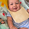 baby, smiling, bib, striped_clothing, baby_seat, animal_print, giraffe, monkey, happy, infant, cute, child, indoor, portrait, plush, seat, comfort, playful, cheerful, young