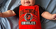 Kyaire is registered to the contest to win money with this photo: baby, infant, child, onesie, clothing, orange, black, person, smile, face, arms, legs, bed, bedsheet, blue, cute, happy, lying_down, indoors, sports_logo