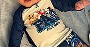 Kyaire is registered to the contest to win money with this photo: baby, child, sunglasses, blue_blanket, paw_patrol, cartoon_clothing, shorts, long_sleeve_shirt, laying_down, indoors, cute, smiling, infant, person, soft_texture, playful, comfortable, relaxed, headwear, cool