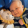 baby, child, plush_toy, lion, smile, striped_clothing, onesie, yellow_trim, blue_background, snuggle, soft_toy, cute, infant, face, happy, cozy, portrait, indoor, person, close_up