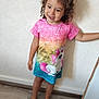 Maddy participe au concours pour gagner de l'argent avec cette photo : child, curly_hair, barefoot, pink_dress, unicorn_print, smiling, standing, indoor, wooden_floor, white_wall, person, cute, happy, casual_clothing, toddler, portrait, young_child, colorful, fashion, playful