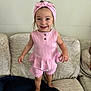 baby, blanket, child, clothing, couch, cute, furniture, girl, happy, headband, home, indoor, person, pink_outfit, playful, portrait, smile, standing, toddler, young_child