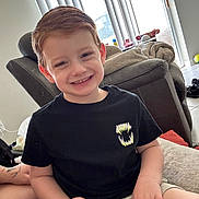 Carter is registered to the contest to win money with this photo: child, boy, smiling, black_tshirt, shorts, indoor, couch, blanket, hair, face, hand, window, vertical_blinds, floor, door, light, home, person, happy, casual