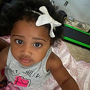 Lyric is registered to the contest to win money with this photo: blanket, bow, carpet, child, curly_hair, expression, eyes, face, floor, girl, gray, home, indoor, person, pink, shirt, sleeveless, toddler, toy, treadmill