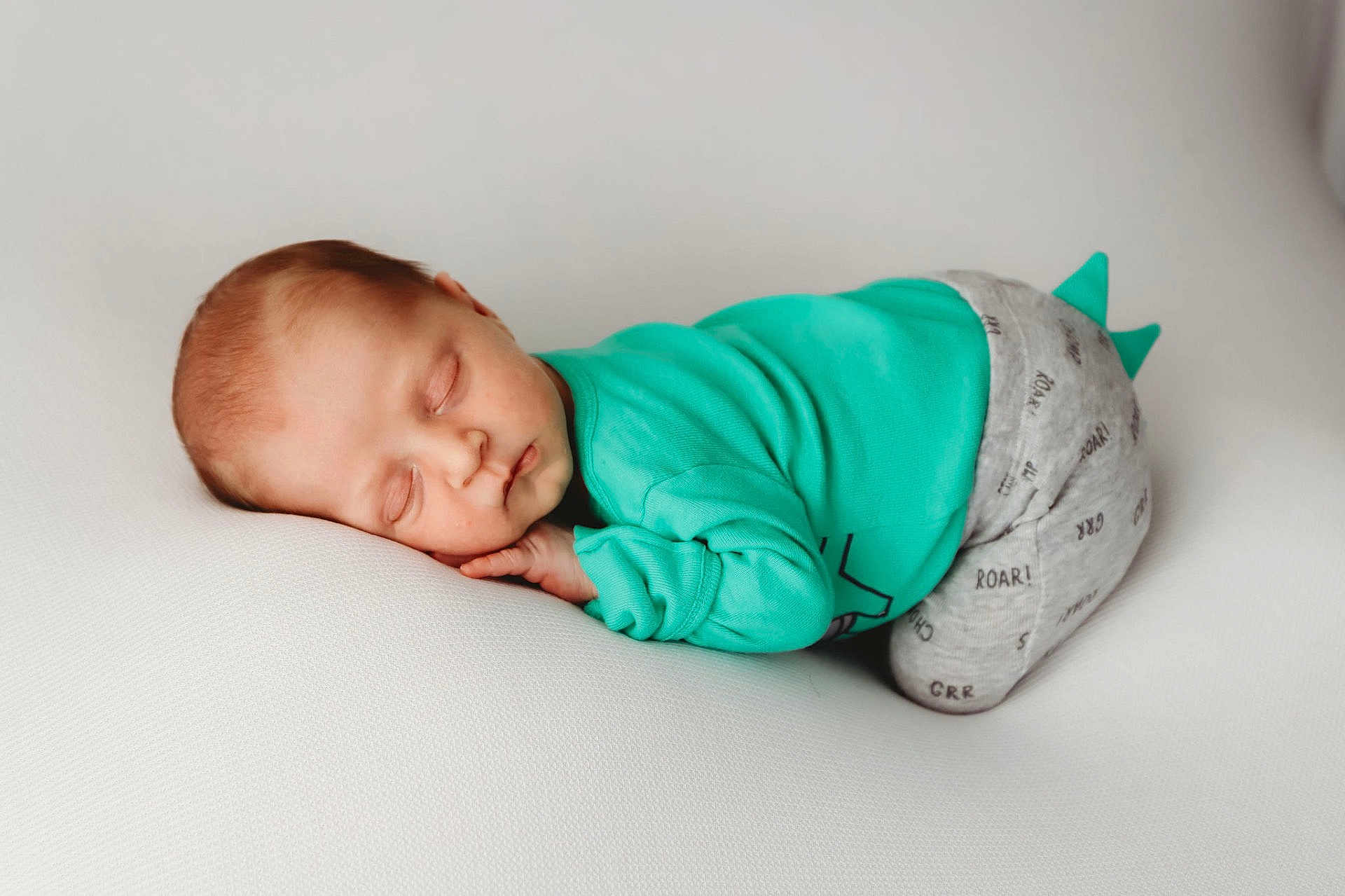 Barrett is registered to the contest to win money with this photo: baby, sleeping, infant, child, cute, turquoise_clothing, gray_pants, spikes, soft_surface, white_background, peaceful, portrait, resting, young_child, newborn, cozy, comfort, face, hand, closed_eyes