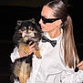 person, dog, pomeranian, bow_tie, white_shirt, black_bow_tie, sunglasses, pony_tail, night, portrait, fashion, pet, holding, cute, fluffy, black, tan, outdoor, stylish, accessory