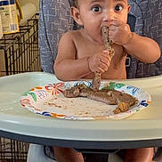 Angelo joined the competition — help win amazing prizes! baby, high_chair, sausage, food, plate, eating, child, indoor, curly_hair, messy, wide_eyes, bare_chest, foot, hand, table, household, mealtime, person, seat, expression