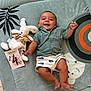 animal_face, baby, bunny, celebration, child, cute, floor, four_months, green_shirt, happy, indoor, infant, lying_down, milestone_card, pattern, play_mat, plush_toy, shorts, smiling, toy
