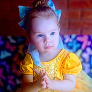 Lue Lue is registered to the contest to win money with this photo: blue_eyes, bow, brick_wall, butterfly_pattern, child, colorful_background, cute, expression, fairy_tale, fashion, girl, hair_bun, hands, indoor, portrait, puffy_sleeves, soft_lighting, toddler, yellow_dress, young