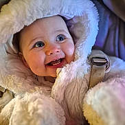 Hartlie is registered to the contest to win money with this photo: baby, child, smiling, hood, fur, coat, blue_eyes, teeth, happy, cute, winter_clothing, infant, portrait, warm, soft_texture, closeup, face, bundle, seatbelt, candid