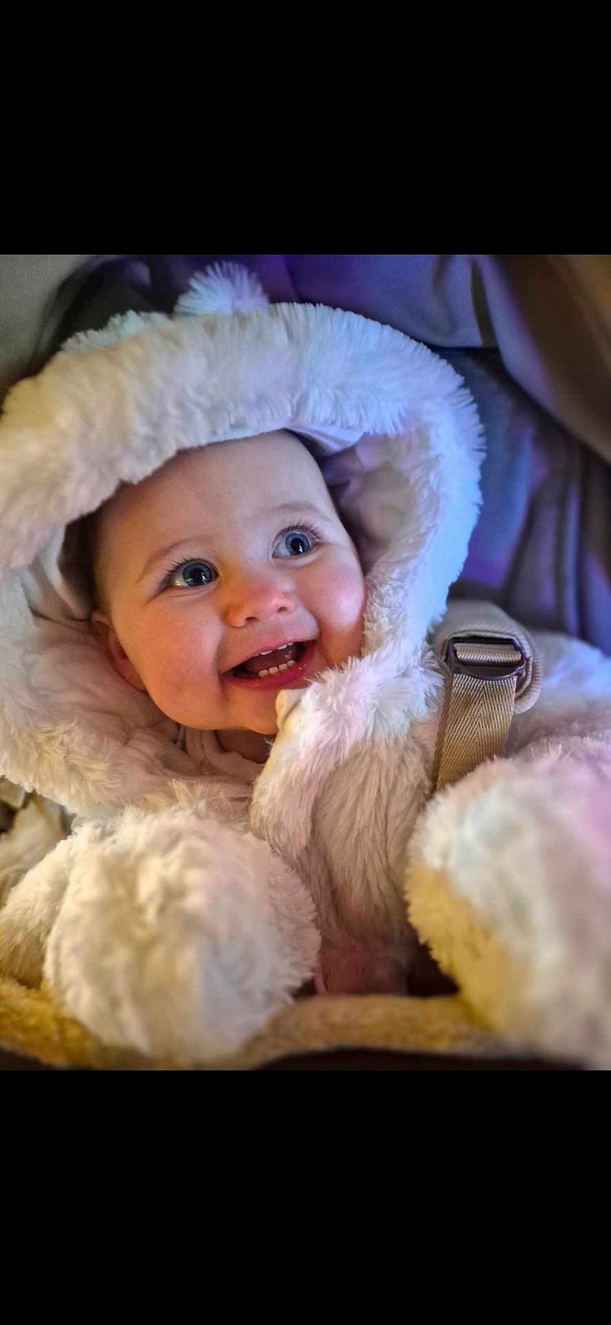 Hartlie is registered to the contest to win money with this photo: baby, child, smiling, hood, fur, coat, blue_eyes, teeth, happy, cute, winter_clothing, infant, portrait, warm, soft_texture, closeup, face, bundle, seatbelt, candid