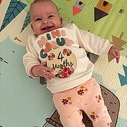 Layana participe au concours pour gagner de l'argent avec cette photo : baby, infant, smiling, play_mat, colorful, clothing, sweater, floral, sign, 4_months, cute, happy, child, person, lying_down, pink_pants, patterned_pants, indoors, cheerful, portrait