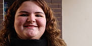 Payton is registered to the contest to win money with this photo: person, face, smile, curly_hair, scarf, portrait, young_person, indoor, brick_wall, casual_clothing, head_and_shoulders, natural_light, friendly_expression, close_up, human, skin, hair, eyebrows, cheeks, nostrils