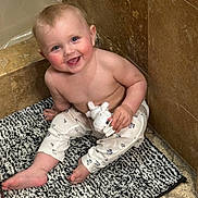 Lindsay is registered to the contest to win money with this photo: baby, infant, child, smile, bathroom, tile, bath_mat, plush_toy, sitting, bare_torso, onesie_pants, chubby_cheeks, blue_eyes, toes, happy, playful, portrait, floor, bathtub_edge, candor