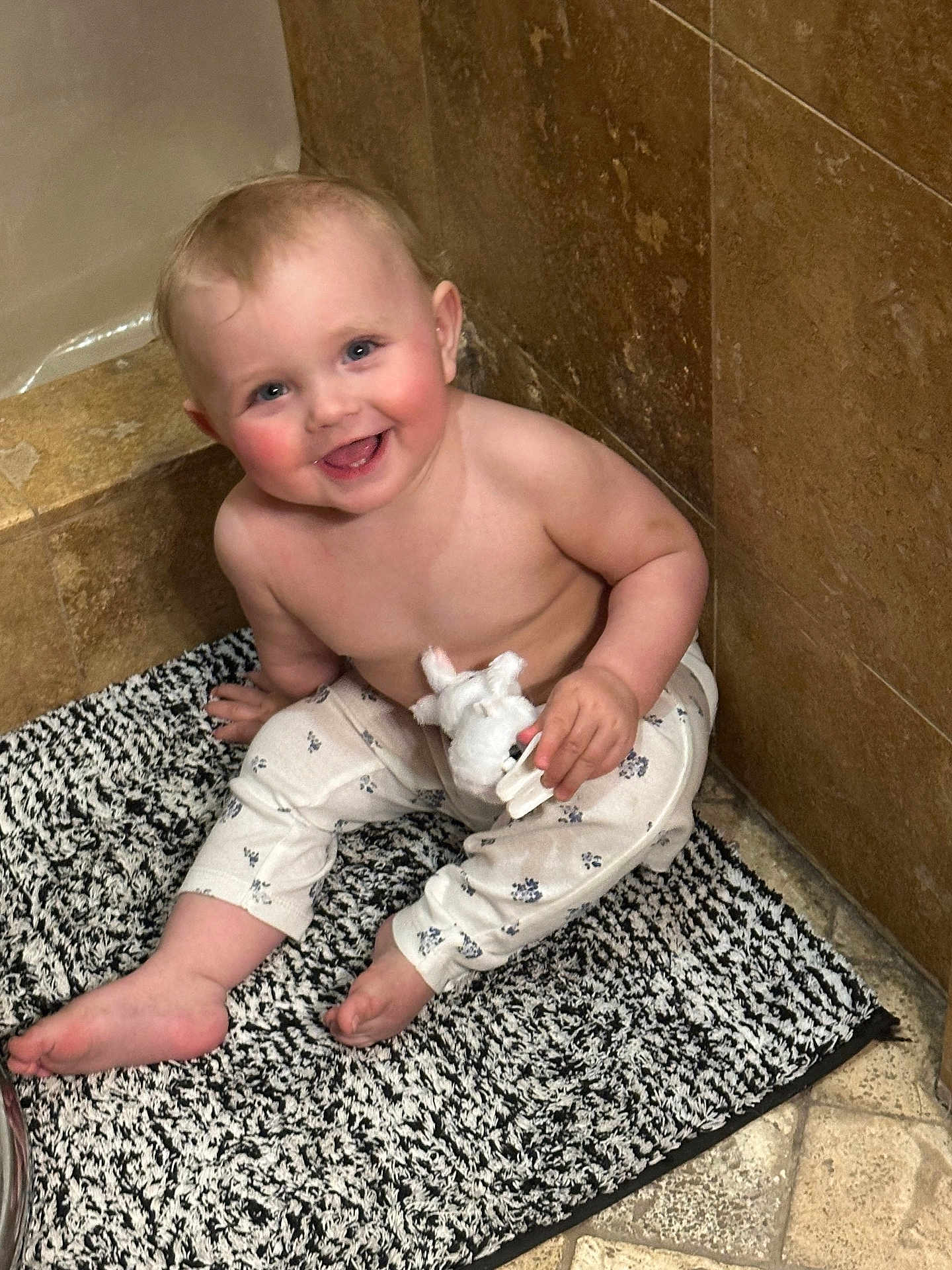 Lindsay is registered to the contest to win money with this photo: baby, infant, child, smile, bathroom, tile, bath_mat, plush_toy, sitting, bare_torso, onesie_pants, chubby_cheeks, blue_eyes, toes, happy, playful, portrait, floor, bathtub_edge, candor