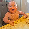 James is registered to the contest to win money with this photo: baby, messy, food, high_chair, smiling, happy, child, indoor, table, face, hands, skin, expression, feeding, cute, infant, clutter, domestic, meal_time, playful