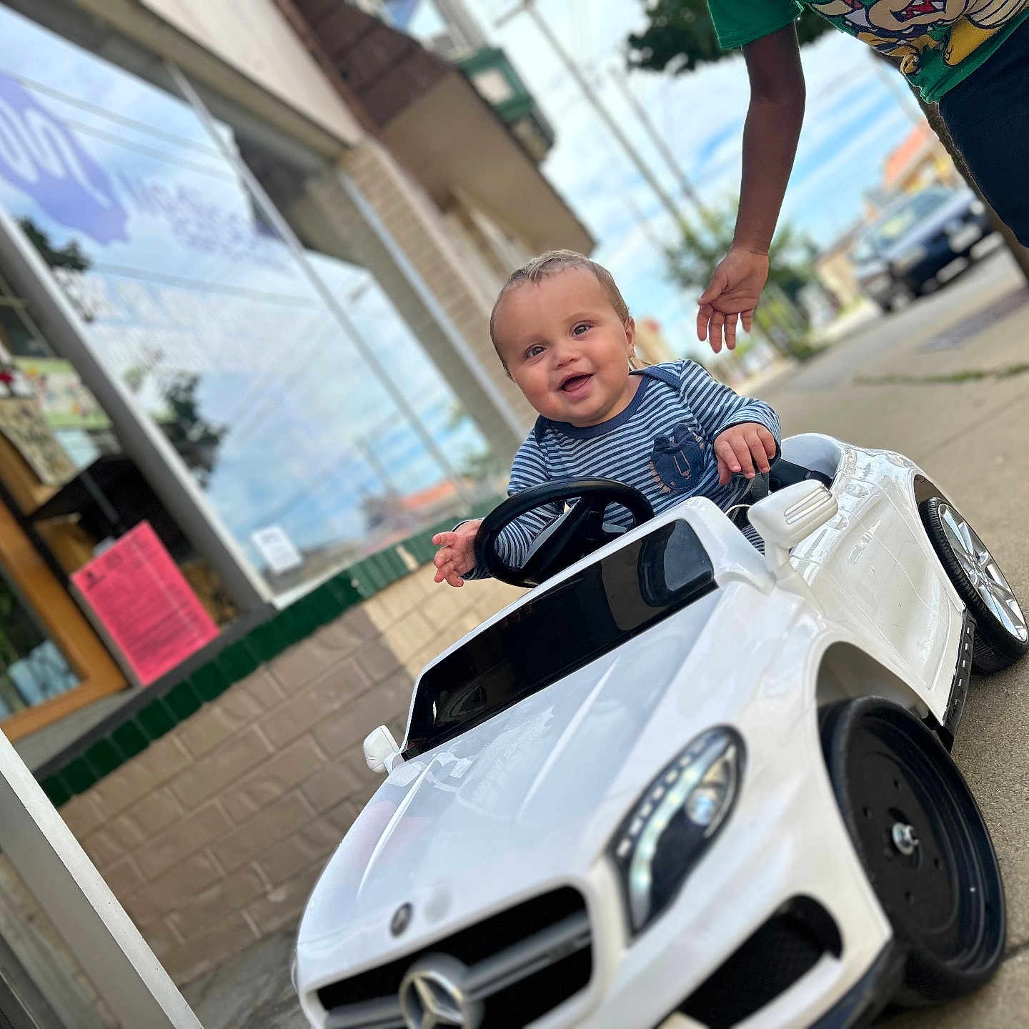 Leonidas is registered to the contest to win money with this photo: baby, building, casual, child, clothing, daylight, door, hand, happy, outdoor, person, play, sidewalk, smiling, street, toy_car, urban, vehicle, white_car, window