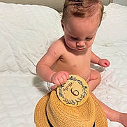 Justin Alexander joined the competition — help win amazing prizes! baby, child, infant, bed, hat, straw_hat, card, months, sitting, white_bed, curious, indoor, person, skin, head, hand, face, young_child, cute, concentration
