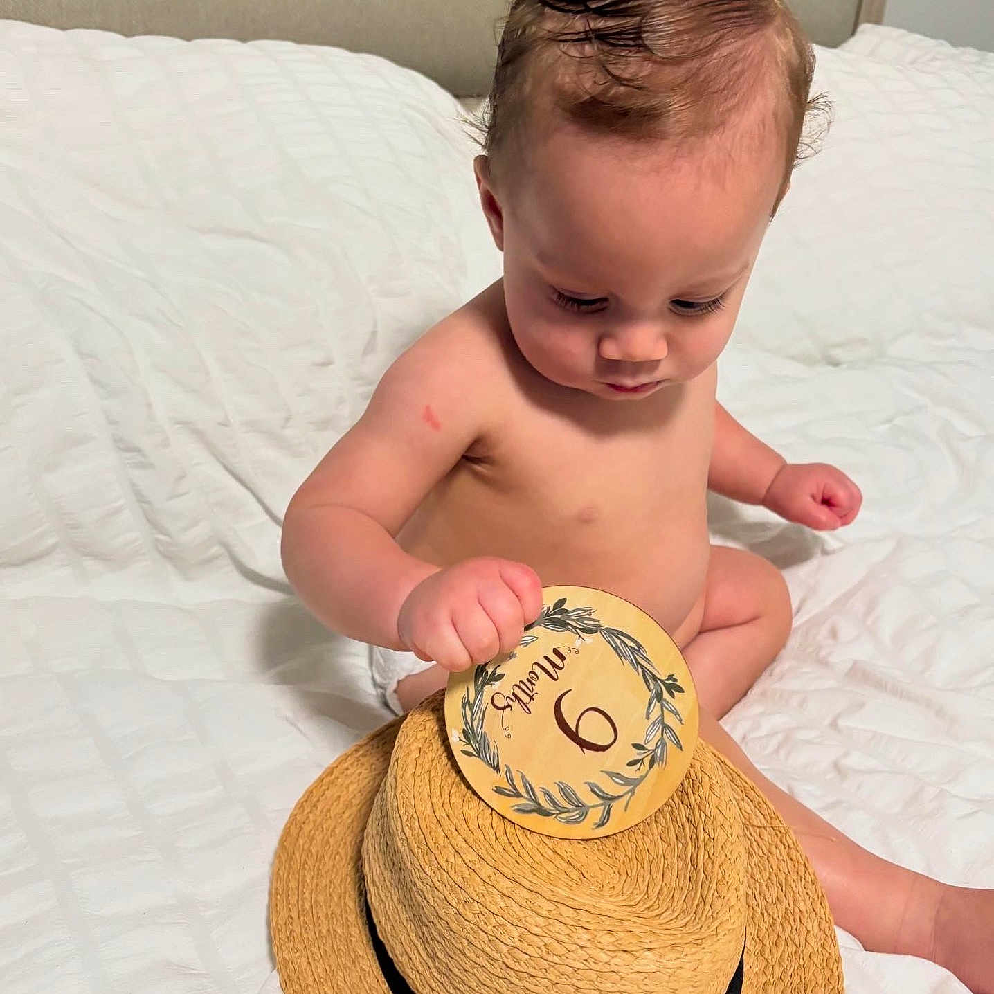 Justin Alexander joined the competition — help win amazing prizes! baby, bed, card, child, concentration, curious, cute, face, hand, hat, head, indoor, infant, months, person, sitting, skin, straw_hat, white_bed, young_child