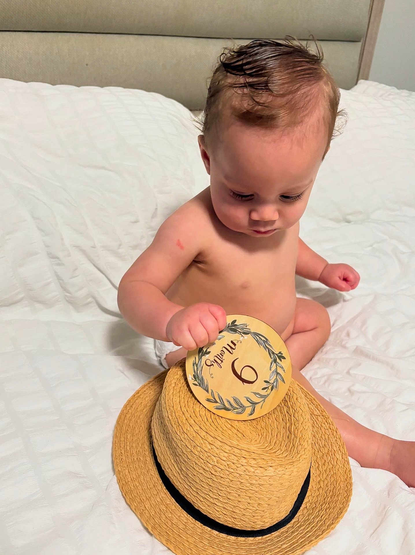 Justin Alexander joined the competition — help win amazing prizes! baby, child, infant, bed, hat, straw_hat, card, months, sitting, white_bed, curious, indoor, person, skin, head, hand, face, young_child, cute, concentration