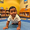 Noah Khalil joined the competition — help win amazing prizes! baby, child, crawling, carpet, library, bookshelf, books, yellow_wall, blue_carpet, indoor, curious, smiling, person, infant, short_hair, casual_clothing, floor, young_child, portrait, playful