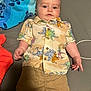 baby, child, dinosaur_shirt, shorts, bed, towel, turtle_pattern, clothing, infant, person, cute, portrait, indoor, lying_down, curious, casual, colorful, young_child, fabric, comfortable