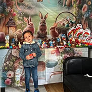 Bruni-Junior a rejoint le concours — aidez-le/la à gagner de superbes lots ! child, denim_jacket, blue_sneakers, easter, bunnies, chocolate, eggs, basket, table, flowers, indoor, smiling, holiday, decorations, person, jeans, wooden_floor, couch, celebration, cute