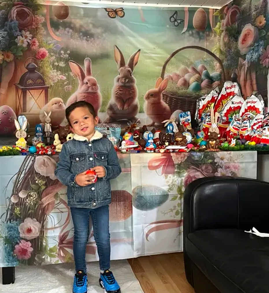 Bruni-Junior a rejoint le concours — aidez-le/la à gagner de superbes lots ! child, denim_jacket, blue_sneakers, easter, bunnies, chocolate, eggs, basket, table, flowers, indoor, smiling, holiday, decorations, person, jeans, wooden_floor, couch, celebration, cute