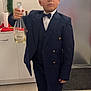 bow_tie, boy, cabinet, celebration, champagne_bottle, child, door, festive, floor, footwear, holding, holiday_decor, indoors, kitchen, person, portrait, serious_expression, standing, suit, young