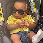 Muhammad joined the competition — help win amazing prizes! baby, child, car_seat, sunglasses, yellow_shirt, blue_shorts, sock, infant, cool, fashion, portrait, cute, seatbelt, hands, legs, indoor, casual, relaxed, young, person
