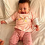 baby, bed, cheerful, child, cute, easter, fabric, happy, indoors, infant, lying_down, pants, pattern, person, pillow, pink_clothing, smile, soft, tshirt, young_child