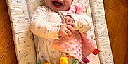 Daisy joined the competition — help win amazing prizes! baby, blanket, bright_colors, child, clothing, cute, face, hands, happy, indoors, infant, joy, lying_down, patterned_mat, playtime, plush_toy, smiling, soft_toy, toddler, wooden_floor