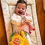 baby, blanket, bright_colors, child, clothing, cute, face, hands, happy, indoors, infant, joy, lying_down, patterned_mat, playtime, plush_toy, smiling, soft_toy, toddler, wooden_floor