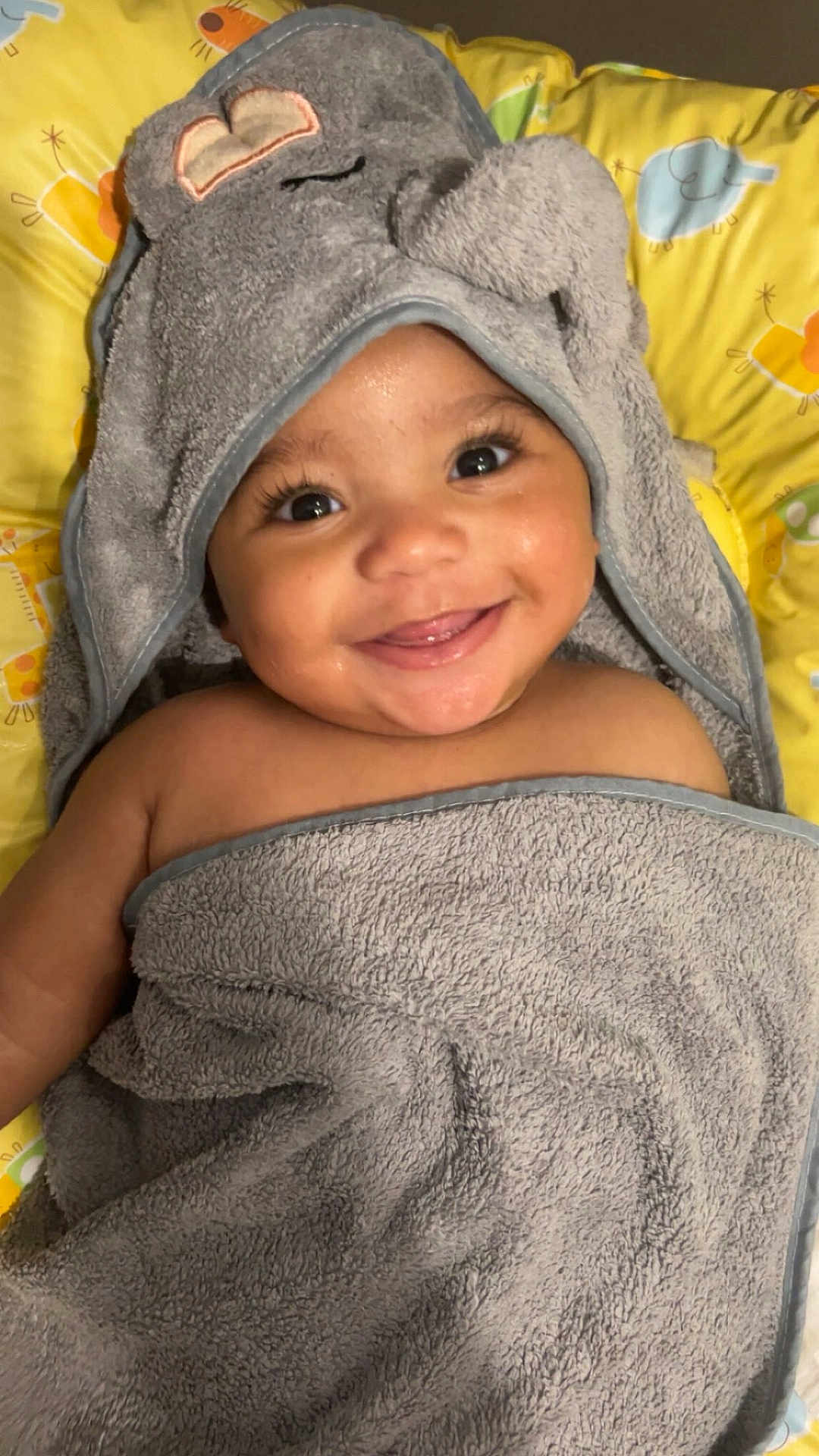 Liyad participe au concours pour gagner de l'argent avec cette photo : baby, infant, smile, towel, hood, elephant_towel, cute, closeup, portrait, wet_skin, cheeks, eyes, eyelashes, yellow_background, baby_bath, blanket, happy, playful, soft_texture, pillow