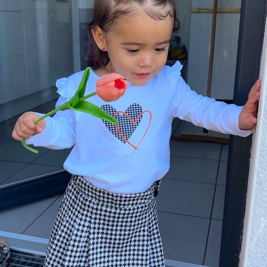 Harmonie participe au concours pour gagner de l'argent avec cette photo : child, cute, doorway, floor, flower, footwear, hair_style, hand, home, indoors, kitchen, light, person, sandals, shirt, skirt, tile, toddler, tulip, window
