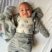 Isaho participe au concours pour gagner de l'argent avec cette photo : baby, infant, smiling, face, clothing, sweatpants, onesie, elephant_plush, soft_toy, bed, sheet, grey, white, cute, lying_down, child, happy, indoor, person, cozy