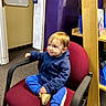 Jackson is registered to the contest to win money with this photo: toddler, child, blue_hoodie, blue_pants, yellow_shoes, office_chair, maroon_chair, carpeted_floor, office, whiteboard, shelf, folders, purple_wall, curly_hair, seated, indoor, person, casual_clothing, young_child, looking_away