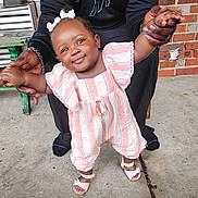 Ariel joined the competition — help win amazing prizes! baby, child, smiling, standing, holding_hands, pink_clothing, striped_clothing, hair_bows, adult_hands, concrete_floor, brick_wall, outdoor, footwear, sandal, cute, person, portrait, happy, support, casual