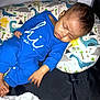 baby, sleeping, blue_onesie, pillow, dinosaur_pattern, blanket, playpen, infant, child, peaceful, indoors, rest, cute, soft_lighting, hand, foot, head, face, cozy, nap