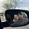 Hazel joined the competition — help win amazing prizes! dog, car_mirror, reflection, hand, smartphone, outdoor, tree, vehicle, window, sky, daylight, parking_lot, road, nature, pet, side_mirror, fur, canine, close_up, leisure