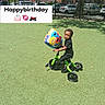 child, tricycle, balloon, outdoor, grass, toy, happybirthday, sesamestreet, green, black_clothing, sunny, daytime, park, play, cute, preschooler, vehicle, smiling, fence, car