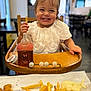 baby_food, child, cute, face, food, french_fries, happy, high_chair, indoor, meal, nuggets, person, playful, restaurant, sippy_cup, smiling, table, toddler, white_clothing, wooden_furniture