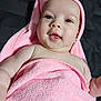 baby, bed, blanket, chubby_cheeks, closeup, cute, earring, eyes, face, hood, indoor, infant, lying_down, mouth, pink_towel, portrait, skin, smile, tongue, towel