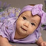 Kelly is registered to the contest to win money with this photo: baby, infant, portrait, closeup, smile, big_eyes, headband, bow, purple_outfit, dress, flower_background, studio_shot, cute, lying_on_stomach, cheeks, soft_texture, earrings, props, adorable, young_child
