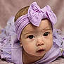 Kelly is registered to the contest to win money with this photo: baby, infant, newborn, headband, bow, purple, dress, eyes, face, portrait, close_up, lying_down, blanket, soft_background, studio_photo, adorable, chubby_cheeks, earring, gaze, skin