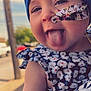 baby, child, face, tongue, headwrap, floral_pattern, medical_tape, dress, arm, outdoor, daylight, person, holding, smiling, cute, skin, closeup, portrait, happy, playful