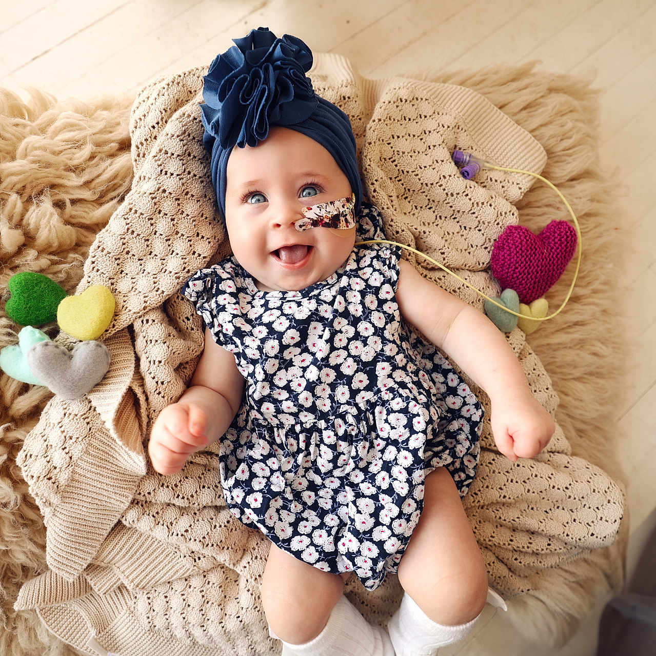 Georgia Ann is registered to the contest to win money with this photo: adorable, baby, blue_eyes, child, colorful, cozy, cute, dress, felt_hearts, flower, happy, headband, indoor, infant, knitted_blanket, lying_down, playful, portrait, smile, soft_texture